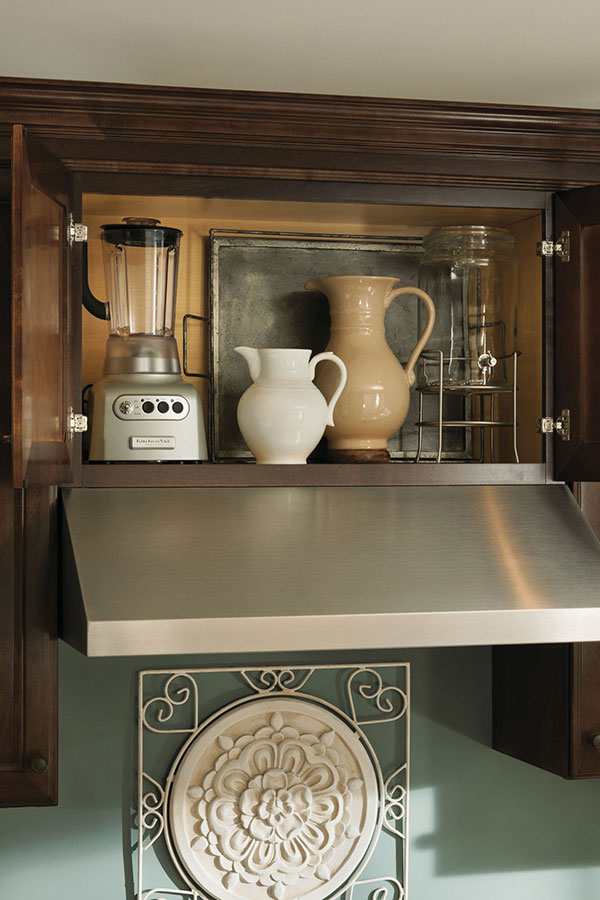 open cabinet above hooded stove holding ceramic jugs and empty blender